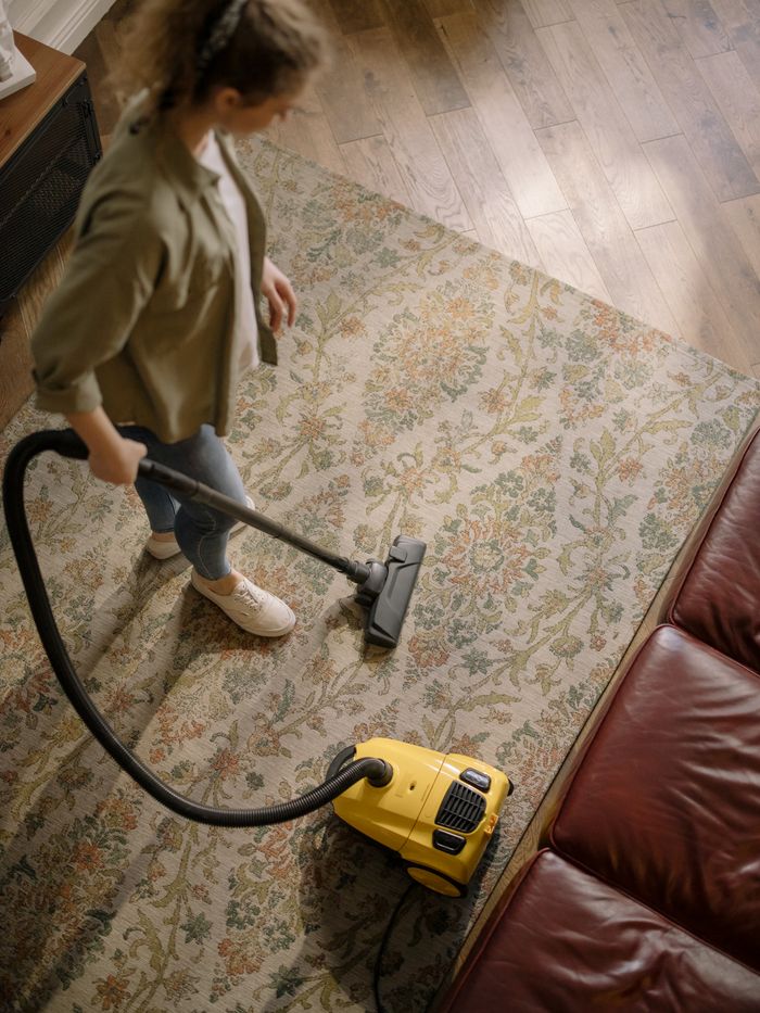 Vue plongeante d’une femme aspirant un tapis chez elle, mettant en avant la propreté et l’entretien ménager.